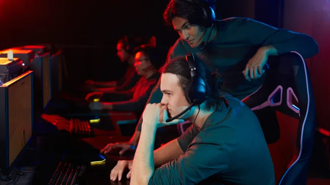Instrutor de esports orientando um jogador concentrado diante do computador durante uma sessão de treinamento.